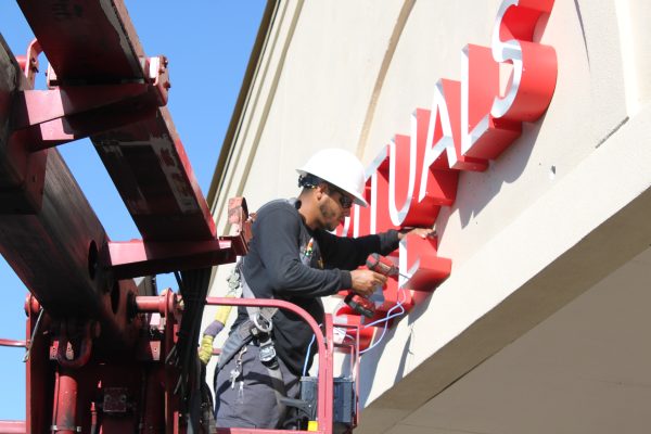 Technician installing illuminated channel letter sign on commercial building exterior