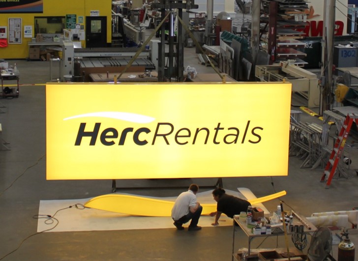 Technicians inspecting illuminated LED signage for Herc Rentals at Thomas Sign & Awning’s Clearwater facility, highlighting energy-efficient sign manufacturing