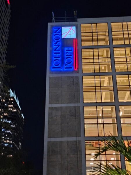 Illuminated building mounted sign for Johnson Pope on high rise office building at night