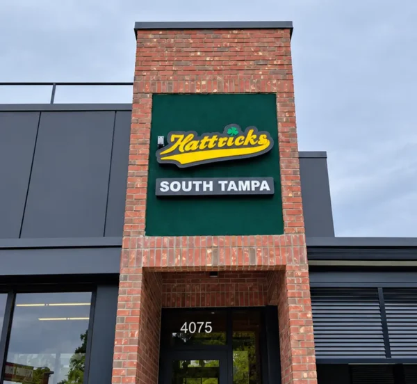 Yellow Hattricks script wall sign and South Tampa lettering above the brick entrance at 4075 Henderson Boulevard