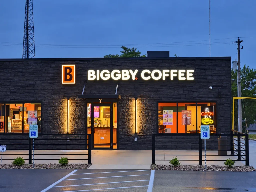Illuminated BIGGBY COFFEE channel letters and orange B logo on a dark brick storefront at dusk